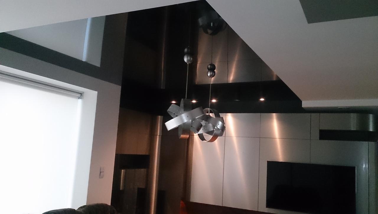 Nowoczesny sufit napinany z połyskiem, podwieszane oświetlenie, metalowe panele ścienne i TV. Minimalistyczny design wnętrza.