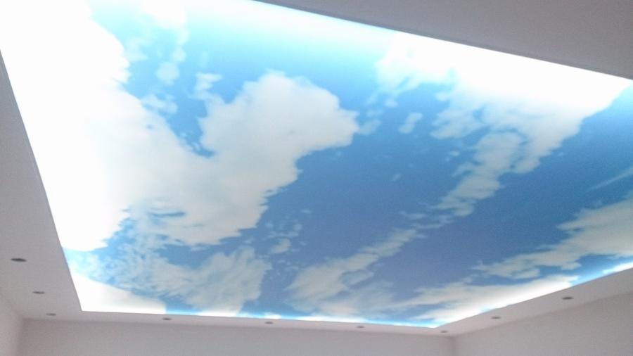 Sufit napinany z motywem błękitnego nieba i chmur, podświetlony, z widocznymi punktowymi oprawami oświetleniowymi w białej ramie sufitu podwieszanego.