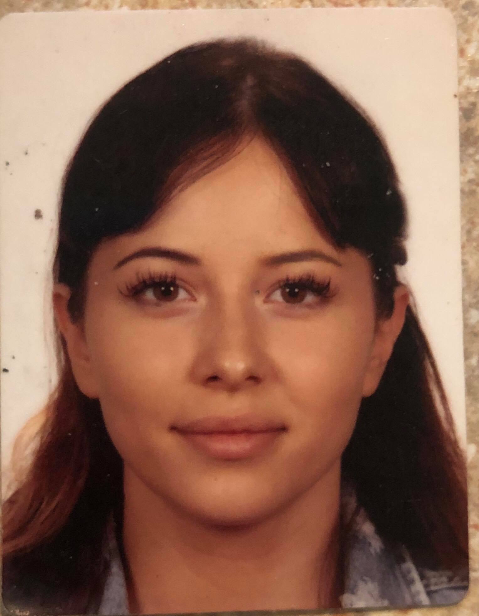 Portret młodej kobiety z ciemnymi włosami i brązowymi oczami, uśmiechająca się delikatnie, na jasnym tle. Widoczne delikatne cieniowanie i naturalny makijaż.