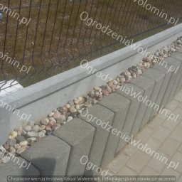 P.P.H.U. WAWMAR MAREK WAWRZONOWSKI - Fragment ogrodzenia z siatki panelowej na betonowej podmurówce, ozdobionej kamieniami rzecznymi, obok ułożona kostka brukowa.
