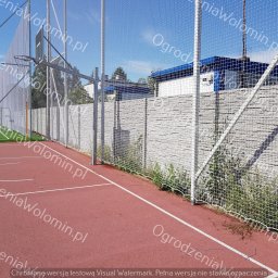 P.P.H.U. WAWMAR MAREK WAWRZONOWSKI - Siatka zabezpieczająca boisko sportowe z koszem do koszykówki, widoczny mur z szarej cegły w tle, trawa i czerwona nawierzchnia boiska.