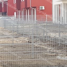 P.P.H.U. WAWMAR MAREK WAWRZONOWSKI - Etap montażu metalowego ogrodzenia z siatki panelowej na nierównym, przygotowywanym terenie działki, widoczne słupki i fragmenty paneli, w tle budynki mieszkalne.