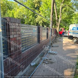 P.P.H.U. WAWMAR MAREK WAWRZONOWSKI - Wznoszona konstrukcja ogrodzenia z ceglanymi słupkami i poziomymi, szarymi panelami, zabezpieczona tymczasową siatką, w tle częściowo widoczny samochód dostawczy i osoba pracująca przy nim.
