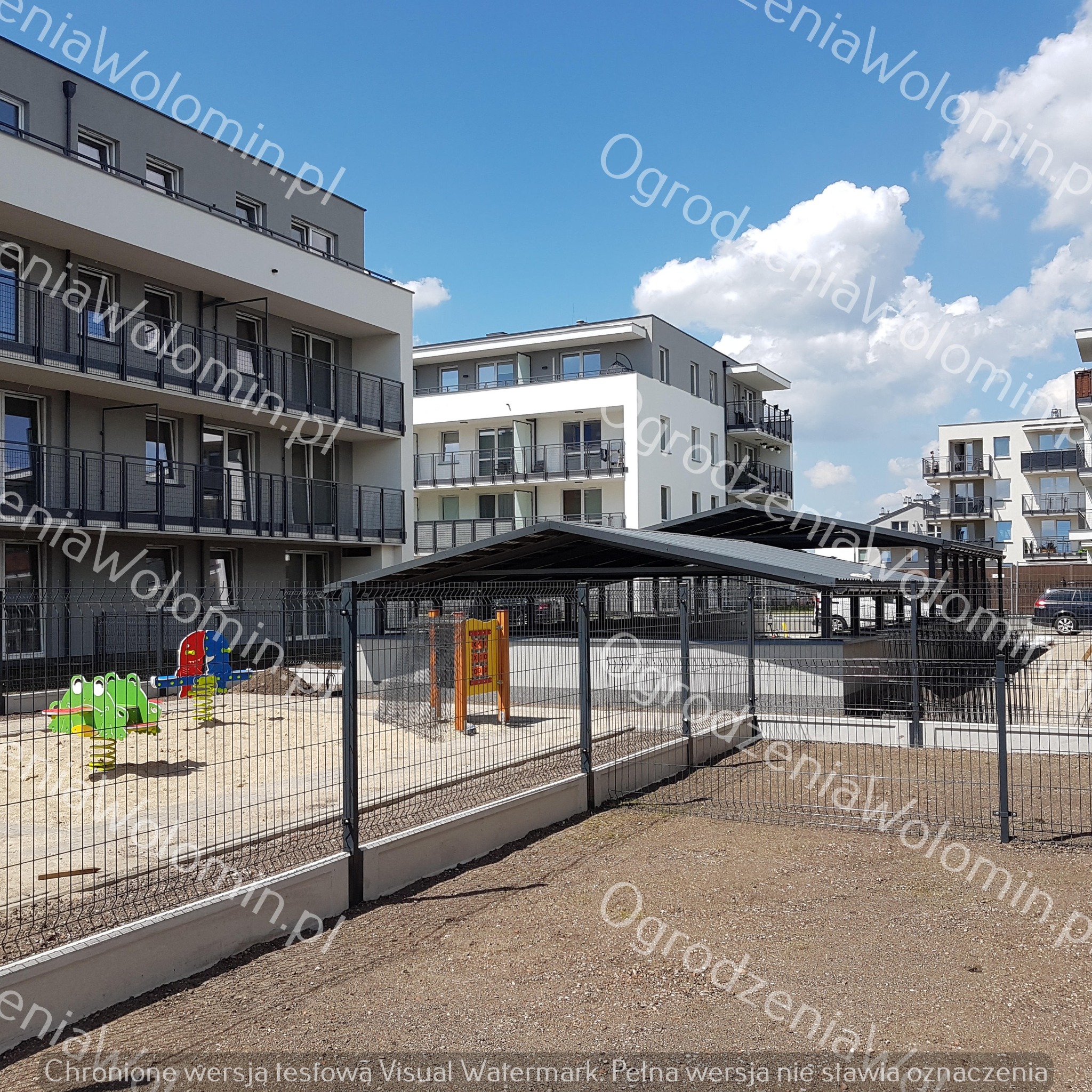 Nowoczesne ogrodzenie panelowe z podmurówką betonową, otaczające plac zabaw na tle budynków mieszkalnych, widoczne sprężynowe zabawki dla dzieci.