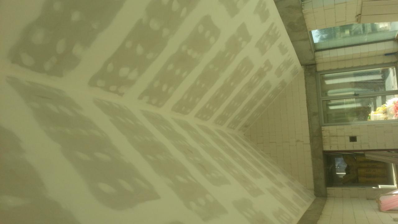 Skośny sufit poddasza w trakcie prac wykończeniowych, widoczne łączenia płyt zaklejone taśmą, przygotowane do dalszej obróbki. W tle okno i fragment muru.