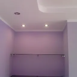 Liliowe ściany z listwami, oświetleniem punktowym i karniszem. Wykończone wnętrze garderoby z delikatnym oświetleniem i subtelną kolorystyką ścian.