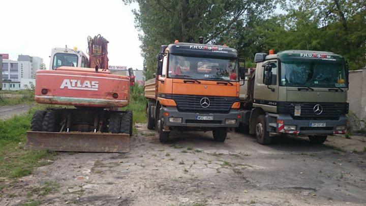 Sprzęt budowlany firmy F.H.U. TOM-MAR Laskowski: koparka Atlas i dwie ciężarówki Mercedes, w tym jedna wywrotka, zaparkowane na placu.