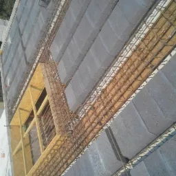 Wiązanie zbrojenia na stropie z bloczków betonowych. Widoczne szalunki okienne z płyty OSB.  Ujęcie z góry, podkreślające regularny układ elementów konstrukcyjnych.