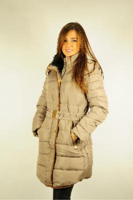 Kobieta w beżowym, pikowanym płaszczu zimowym z futrzanym kołnierzem i paskiem w talii, pozująca na jednolitym tle.