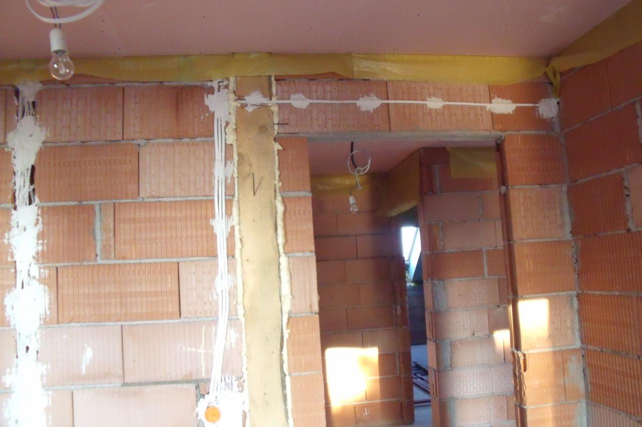 Wewnętrzne ściany z cegły z widocznymi przewodami elektrycznymi przytwierdzonymi gipsem, surowy stan, żarówka na kablu zwisająca z sufitu.