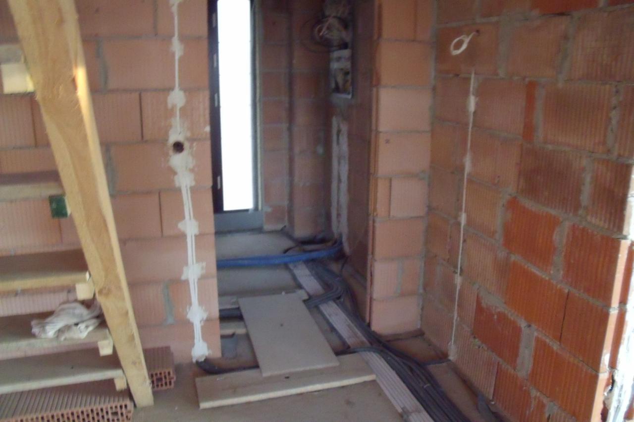 Instalacja elektryczna w surowym wnętrzu: kable w ścianach z cegły, przewody pod podłogą, widoczne puszki. Etap prac wykończeniowych w nowym budynku.