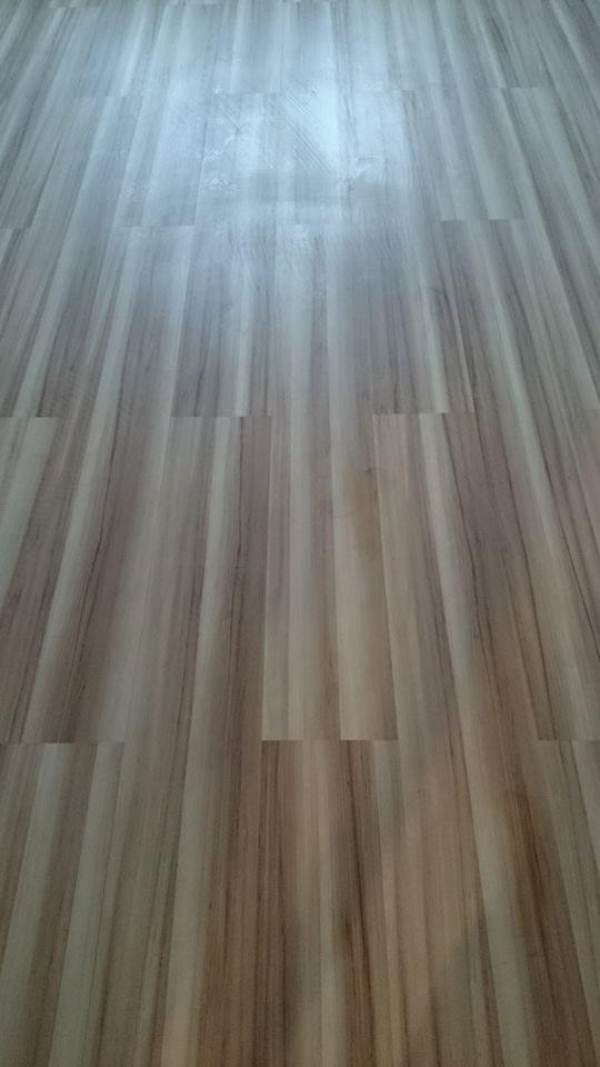 Ułożona podłoga z paneli imitujących drewno, z widoczną strukturą słojów, ułożona wzdłużnie, z delikatnym połyskiem, w ciepłej tonacji kolorystycznej.