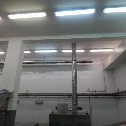 Wnętrze przemysłowe z białymi panelami ściennymi, metalowymi rurami i oświetleniem sufitowym. Widoczna maszyna Cryovac i elementy instalacji technologicznej.