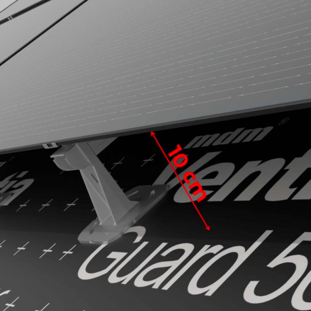 Szary panel słoneczny zamontowany na czarnej membranie dachowej z widocznym wspornikiem montażowym i czerwoną strzałką wskazującą odległość 10 cm.