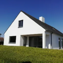 Nowoczesny dom jednorodzinny z białą elewacją i grafitowymi oknami, otoczony zielonym żywopłotem, widok w słoneczny dzień.