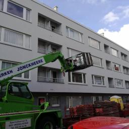 Sevo - Szary budynek wielorodzinny po tynkowaniu elewacji, widok z poziomu podnośnika koszowego firmy Dakwerken Jonckheere, z paletami materiałów budowlanych w tle.