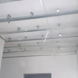 EKO-INSTAL PIOTR BAJOR - Stelaż sufitowy z płyt karton-gips, widoczne profile metalowe, uchwyty montażowe i przewody instalacji elektrycznej, przygotowany do montażu płyt.