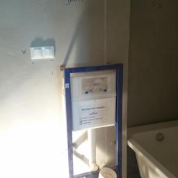 EKO-INSTAL PIOTR BAJOR - Stelaż podtynkowy Cersanit zamontowany w łazience w trakcie remontu, widoczna instalacja hydrauliczna, fragment wanny i włącznik światła na ścianie.