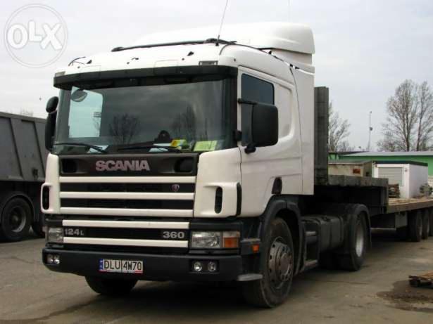 Biała ciężarówka Scania 124L 360 z platformą lawety, widoczny numer rejestracyjny DLU 4W70, zaparkowana na placu.