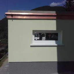 Elewacja budynku w Osieku z oknem i miedzianym orynnowaniem, widoczna faktura tynku i fragment chodnika.