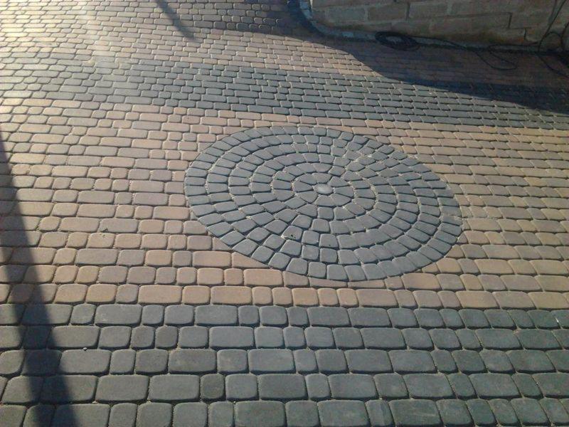 Ułożona nawierzchnia z kostki brukowej w dwóch odcieniach szarości i beżu, tworząca dekoracyjny wzór okręgu na środku.