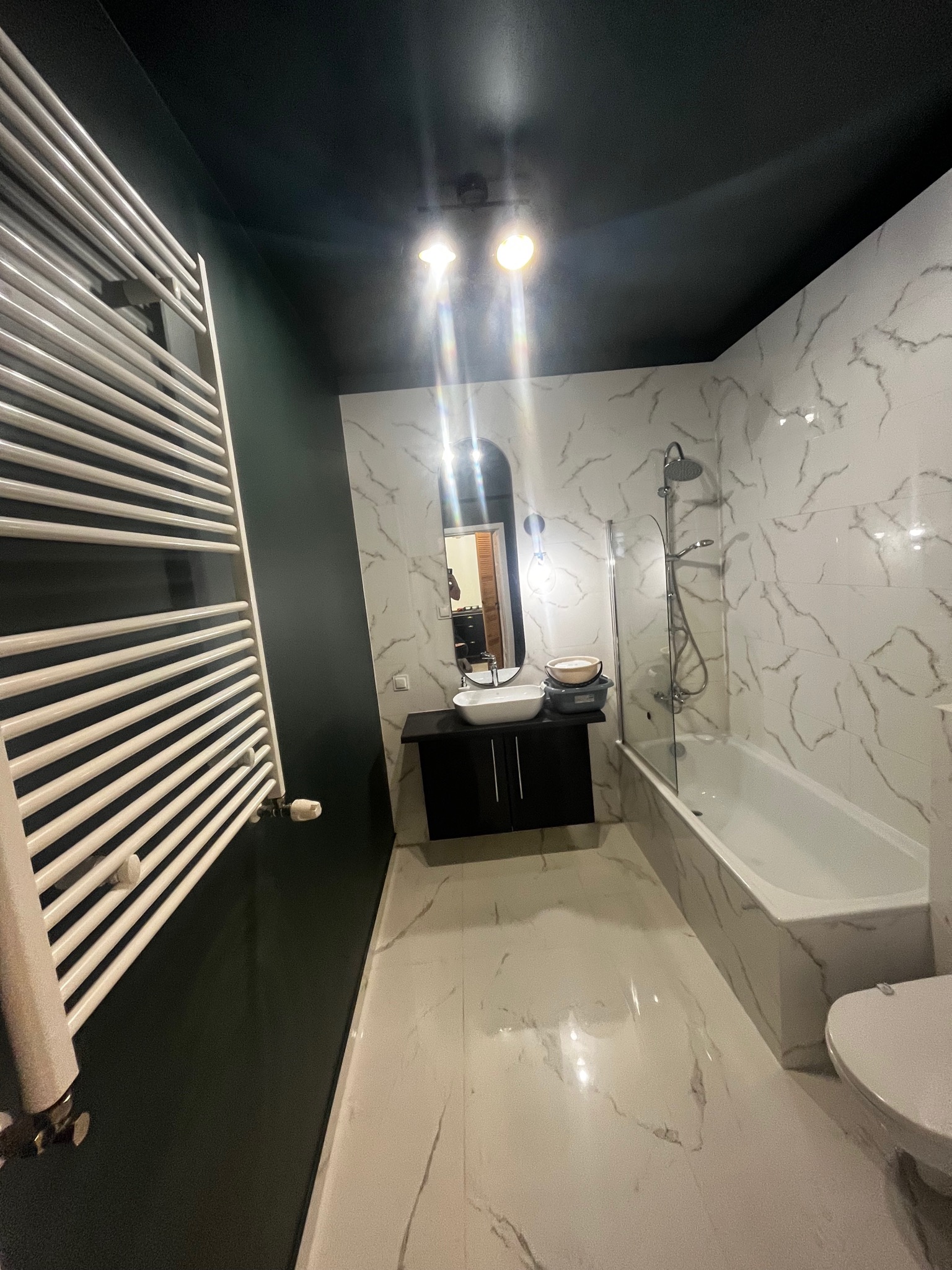 Nowoczesna łazienka z czarnym sufitem, marmurowymi płytkami, grzejnikiem drabinkowym i umywalką nablatową.