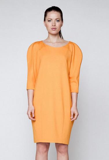 Modelka prezentuje pomarańczową sukienkę o prostym kroju z rękawami 3/4 i bufkami na ramionach na neutralnym tle. Sukienka damska.