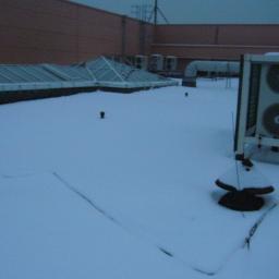 SIMPLEC-SERVICE Profesjonalne-Usługi-Porządkowe - Zasypany śniegiem dach budynku z widocznymi świetlikami, wentylacją i klimatyzacją. Zimowy krajobraz miejski z elementami infrastruktury technicznej.