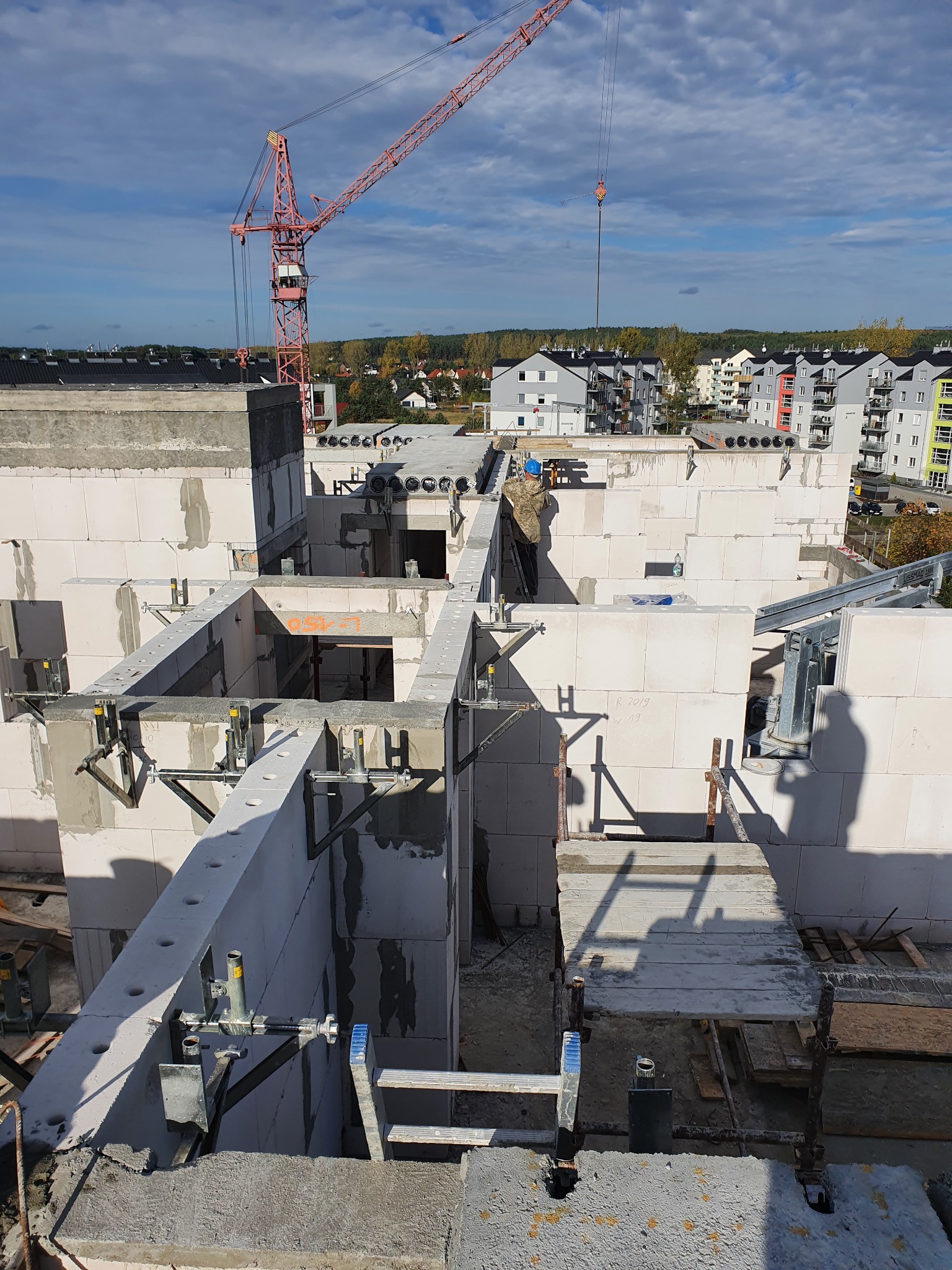Wznoszenie murów z betonu komórkowego na budowie wielorodzinnego budynku mieszkalnego, widoczny czerwony żuraw i okoliczna zabudowa.