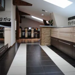 Nowoczesna kuchnia w skosach, z dwukolorowymi frontami szafek i kontrastującą podłogą. Widoczne drewniane elementy konstrukcyjne i kamienna kolumna.