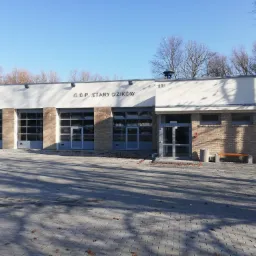 Nowo wybudowana remiza strażacka OSP Stary Dzików z trzema bramami garażowymi, murowana z jasnej cegły, z numerem 101 nad wejściem, oświetlona porannym słońcem.