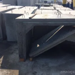 Betonowe prefabrykaty: elementy przepustów skrzynkowych z uchwytami transportowymi, składowane na placu budowy, z widoczną konstrukcją wewnętrzną jednego elementu.