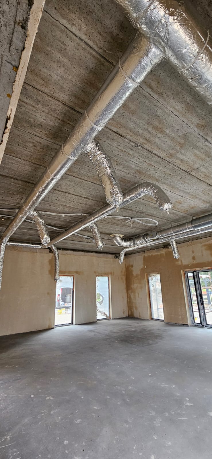 Instalacja wentylacyjna z aluminiowymi rurami pod sufitem surowego biura z widocznymi przewodami i otworami wentylacyjnymi.