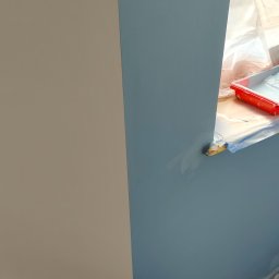 NewLifeColor MAREK BECHT Malowanie Mieszkań i Domów - Ściana pomalowana na dwa kolory: beżowy i niebieski. Widoczny wałek malarski i zabezpieczone okno folią. Świeżo pomalowane powierzchnie, wyraźne odcięcie kolorów.