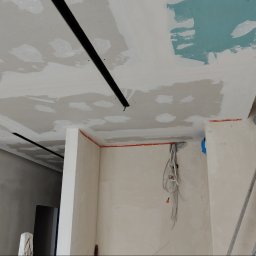 NewLifeColor MAREK BECHT Malowanie Mieszkań i Domów - Sufit z płyt gipsowo-kartonowych w trakcie szpachlowania, widoczne czarne listwy oświetleniowe, instalacja elektryczna i fragment drabiny malarskiej.