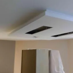 Pomieszczenie z kremowymi ścianami i białym sufitem podwieszanym z dwoma prostokątnymi otworami na oświetlenie.