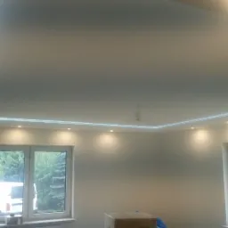 Nowoczesny sufit podwieszany z oświetleniem LED punktowym i paskowym, widok z dołu, kartonowe pudło na podłodze, drabina oparta o ścianę przy oknie.