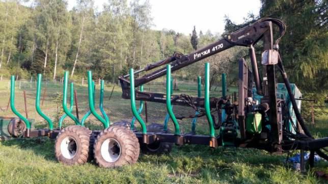 Przyczepa leśna z żurawiem hydraulicznym na łące, gotowa do załadunku drewna.