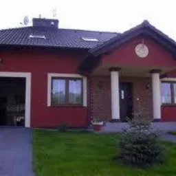 Dom jednorodzinny z czerwoną elewacją, białymi kolumnami przy wejściu i otwartym garażem z widocznym wnętrzem.