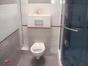 Nowoczesna toaleta podwieszana w łazience z szarymi i białymi płytkami, dekoracyjnym motywem kwiatowym nad spłuczką oraz kabiną prysznicową w tle.