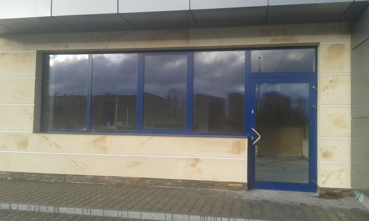 Elewacja budynku z oknami i drzwiami w niebieskich ramach. Dekoracyjna faktura ściany w odcieniach beżu i brązu. Widoczne elementy wykończeniowe.