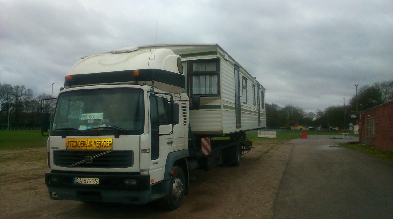 Ciężarówka Volvo z naczepą przewożąca mobilny dom na platformie, widok z przodu na tle pochmurnego nieba.