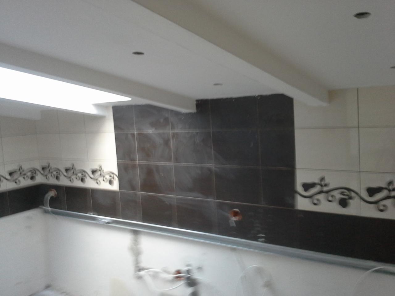 Fragment ściany w łazience z ułożonymi płytkami w odcieniach bieli i brązu, dekoracyjnym motywem roślinnym i widoczną instalacją. Wnętrze w trakcie wykończenia.