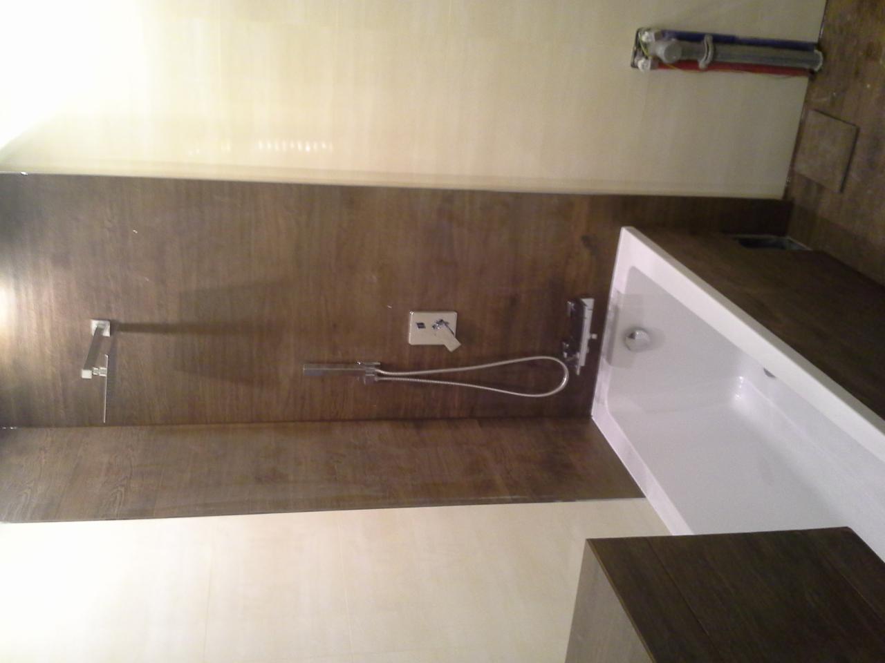 Nowoczesna łazienka z wanną, panelami ściennymi imitującymi drewno i chromowaną armaturą. Widoczne przyłącza wodne. Ujęcie z góry.