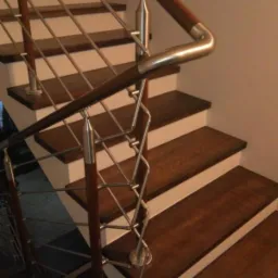 Schody z drewnianymi stopniami, białymi podstopnicami i metalową balustradą o dekoracyjnym wzorze, widziane z dołu pod kątem.