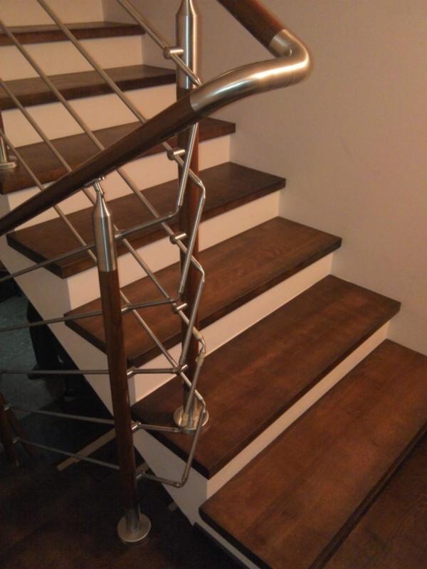 Nowoczesne schody z drewnianymi stopniami i metalową balustradą. Elementy ze stali nierdzewnej i drewniane poręcze. Widok z dołu, oświetlenie ciepłe.
