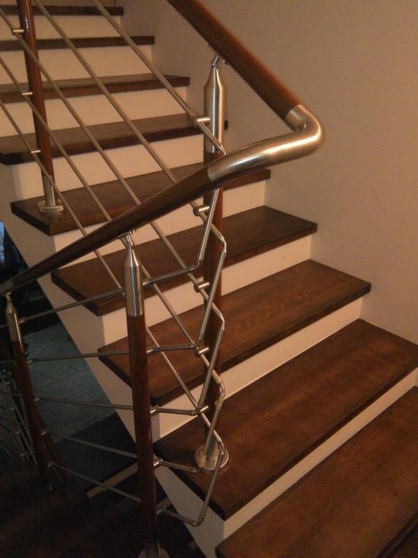Schody z drewnianymi stopniami, białymi podstopnicami i metalową balustradą o dekoracyjnym wzorze, widziane z dołu pod kątem.
