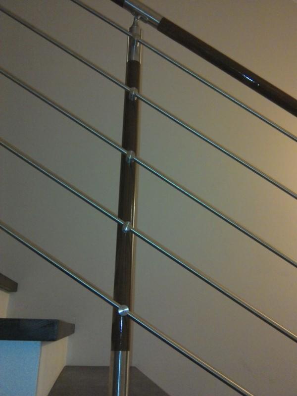 Nowoczesna balustrada schodowa z drewnianymi elementami i metalowymi, poziomymi prętami, zamontowana wewnątrz budynku, widok z dołu.