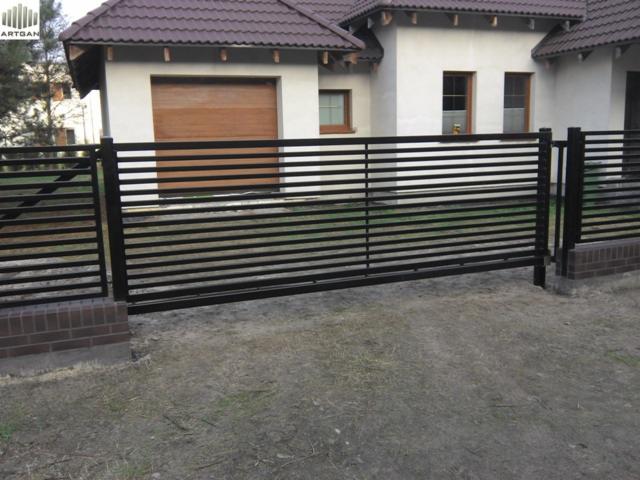 Nowoczesne, poziome ogrodzenie metalowe w kolorze czarnym, z widocznym domem jednorodzinnym w tle. Minimalistyczny design, eleganckie wykończenie.