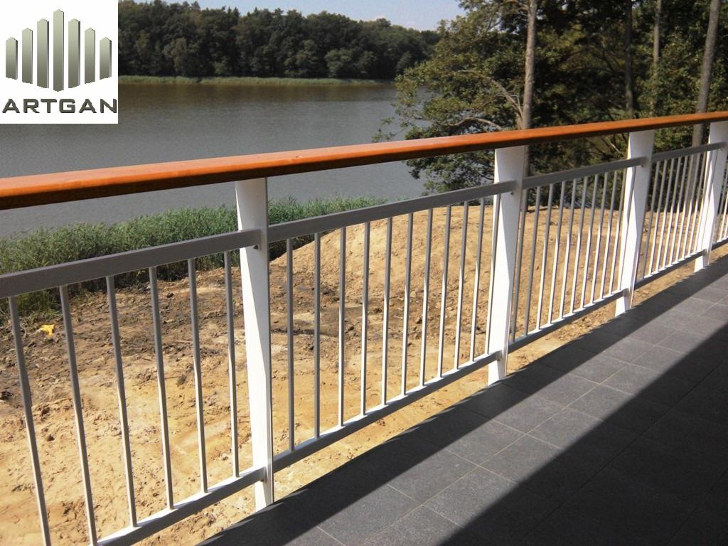 Barierka metalowa z drewnianym wykończeniem w Dąbrowie Chełmińskiej, widok na jezioro. Nowoczesne, białe słupki i szare pręty tworzą minimalistyczny design.